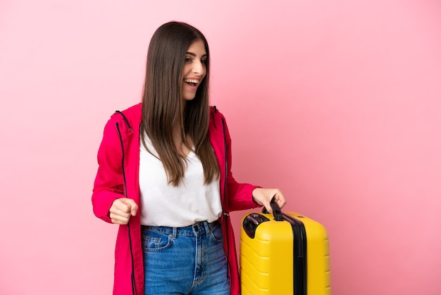 Giovane donna caucasica isolata su sfondo rosa in vacanza con valigia da viaggio