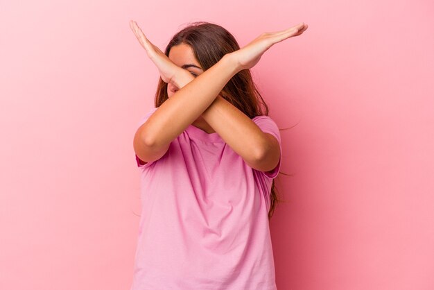 Giovane donna caucasica isolata su sfondo rosa mantenendo due braccia incrociate, concetto di negazione.