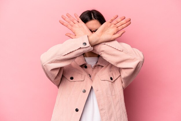 Giovane donna caucasica isolata su sfondo rosa mantenendo due braccia incrociate concetto di negazione