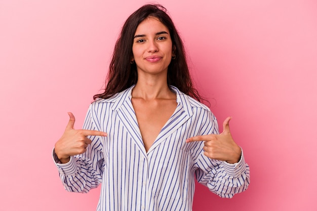 Giovane donna caucasica isolata su sfondo rosa persona che indica a mano uno spazio copia camicia, orgogliosa e fiduciosa