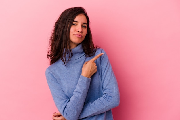 Giovane donna caucasica isolata su sfondo rosa sorridente e puntata da parte, mostrando qualcosa in uno spazio vuoto.