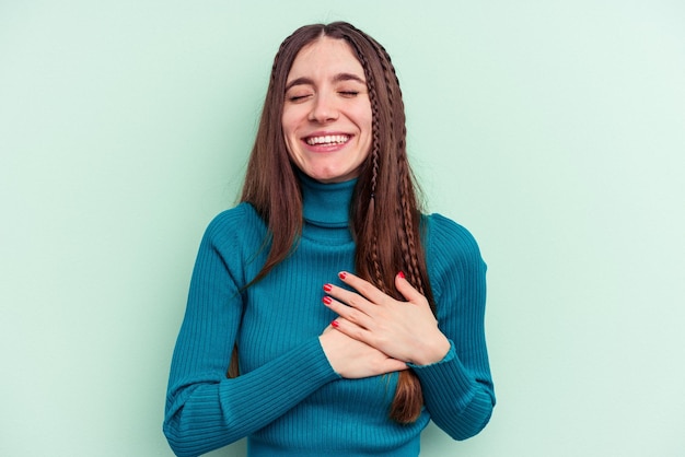 Giovane donna caucasica isolata su sfondo verde che ride tenendo le mani sul concetto di felicità del cuore