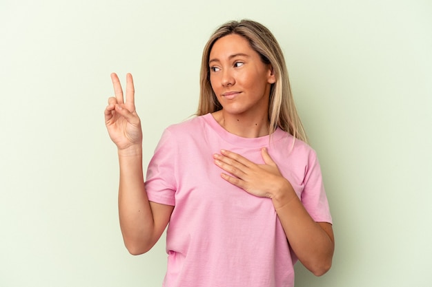 Giovane donna caucasica isolata su sfondo verde prestando giuramento, mettendo la mano sul petto.