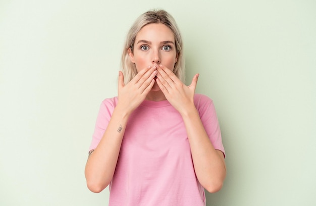 Giovane donna caucasica isolata su sfondo verde scioccata che copre la bocca con le mani.