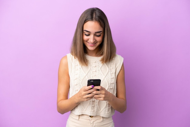 Giovane donna caucasica isolata su sfondo viola che invia un messaggio con il cellulare