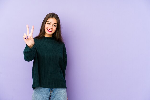 Giovane donna caucasica isolata su sfondo viola che mostra il numero due con le dita.