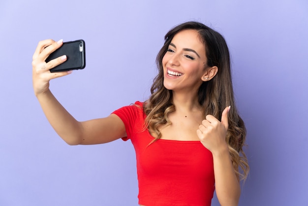 Giovane donna caucasica isolata su sfondo viola facendo un selfie con il telefono cellulare