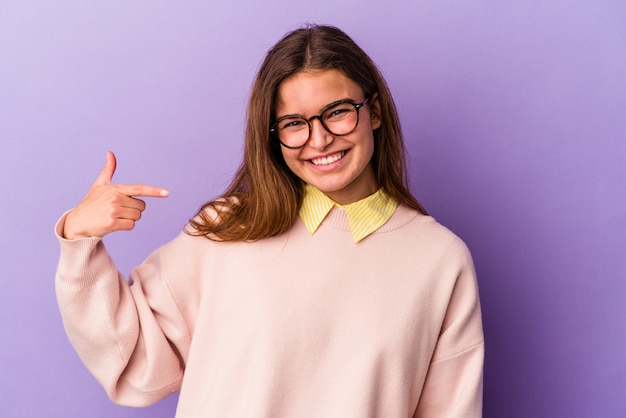 Giovane donna caucasica isolata su sfondo viola persona che indica a mano uno spazio copia camicia, orgogliosa e fiduciosa