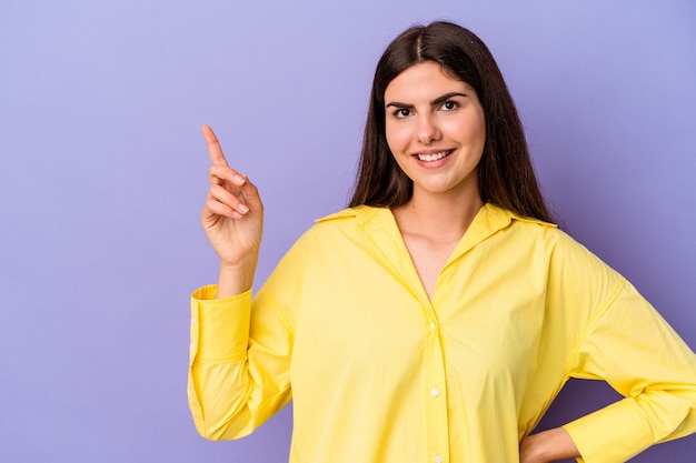 Giovane donna caucasica isolata su sfondo viola sorridente allegramente puntando con l'indice lontano.