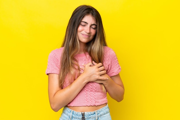 Giovane donna caucasica isolata su uno sfondo giallo con un dolore nel cuore