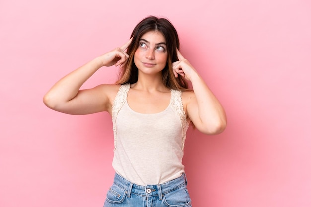 Giovane donna caucasica isolata su uno sfondo rosa con dubbi e pensieri