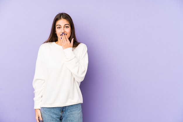 Giovane donna caucasica isolata su viola scioccata, coprendo la bocca con le mani, ansiosa di scoprire qualcosa di nuovo.