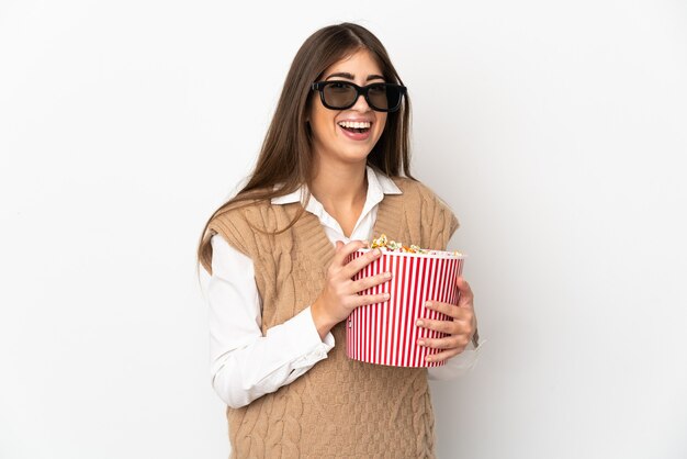 Giovane donna caucasica isolata sul muro bianco con gli occhiali 3d e che tiene un grande secchio di popcorn