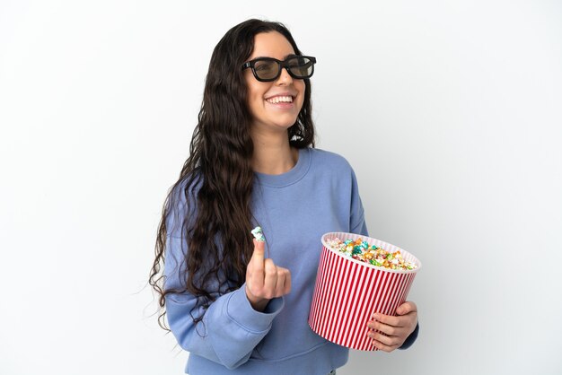 Giovane donna caucasica isolata sul muro bianco con occhiali 3d e che tiene un grande secchio di popcorn