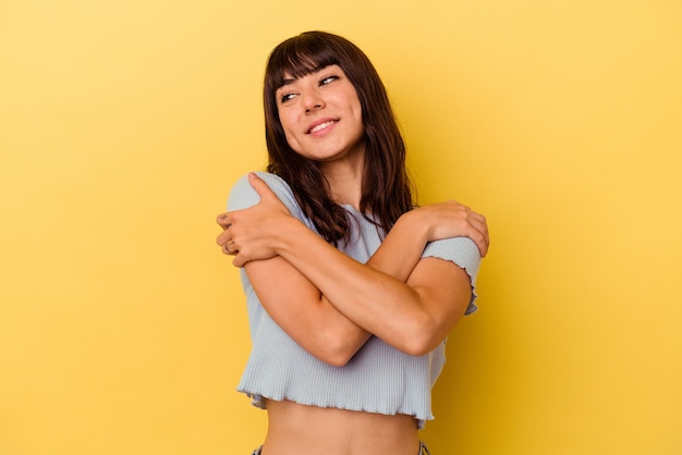 Giovane donna caucasica isolata sul muro giallo abbracci, sorridente spensierata e felice.