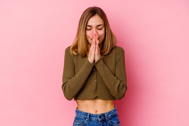 Giovane donna caucasica isolata sul muro rosa con le mani in preghiera vicino alla bocca, si sente sicura.