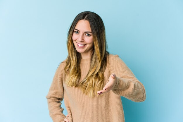 Giovane donna caucasica isolata sull'azzurro che allunga la mano nel gesto di saluto.