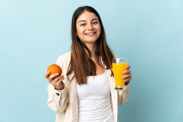 Giovane donna caucasica isolata sull'azzurro che tiene un'arancia e un succo d'arancia