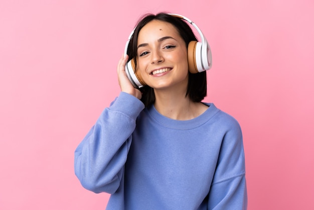 Giovane donna caucasica isolata sulla musica d'ascolto della parete rosa