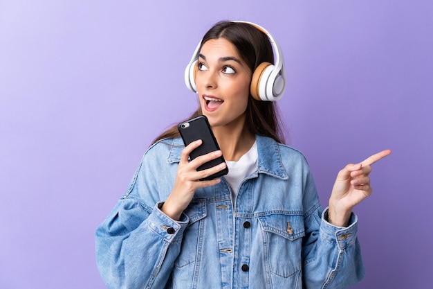 Giovane donna caucasica isolata sulla musica d'ascolto viola con un cellulare e cantando