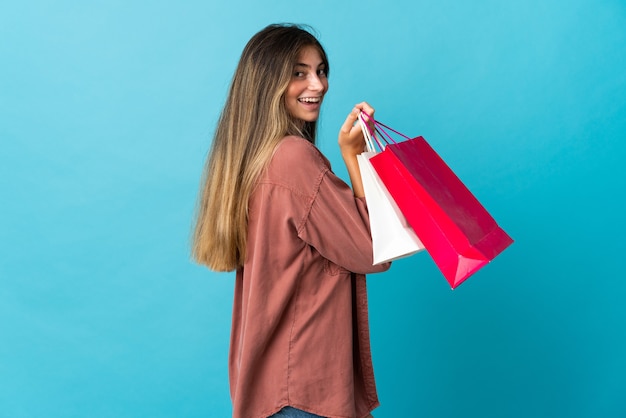 Giovane donna caucasica isolata sulla parete blu che tiene i sacchetti della spesa e sorridente