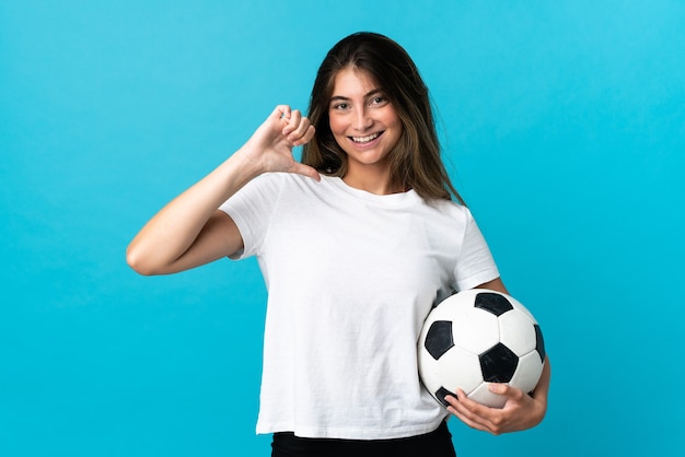 Giovane donna caucasica isolata sulla parete blu con pallone da calcio e orgoglioso di se stesso