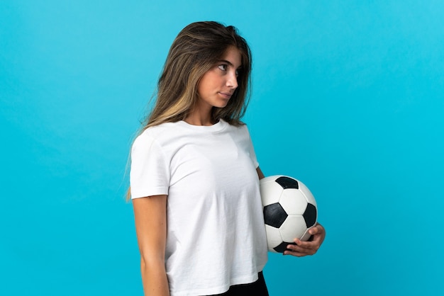 Giovane donna caucasica isolata sulla parete blu con pallone da calcio