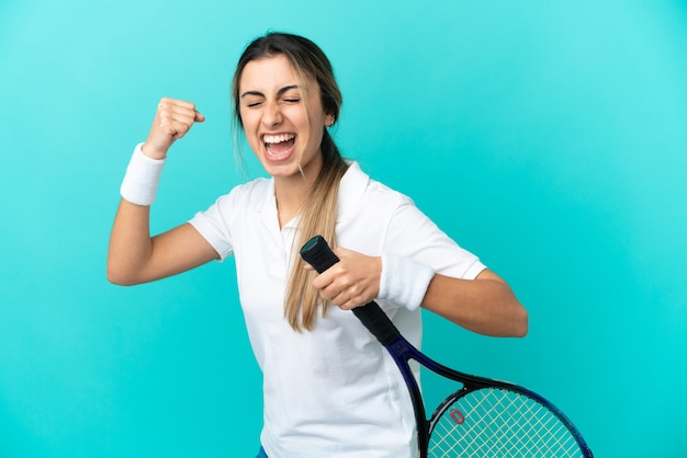 Giovane donna caucasica isolata sulla parete blu, giocare a tennis e celebrare una vittoria