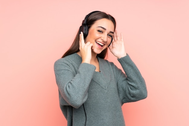 Giovane donna caucasica isolata sulla parete rosa che ascolta musica e canto