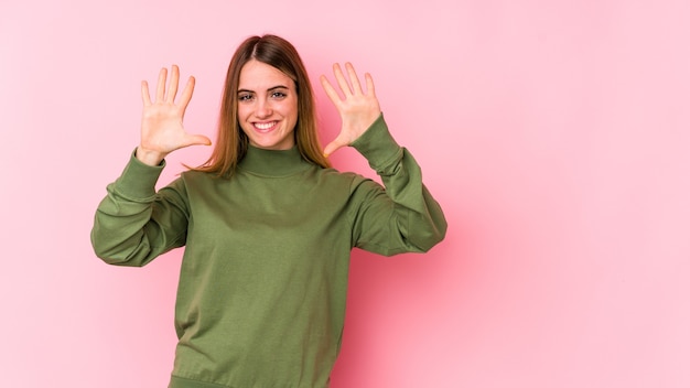 Giovane donna caucasica isolata sulla parete rosa che mostra il numero dieci con le mani.