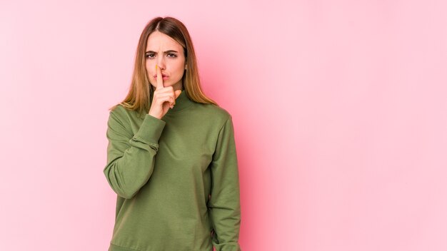 Giovane donna caucasica isolata sulla parete rosa mantenendo un segreto o chiedendo silenzio.