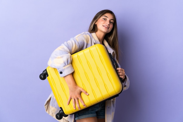Giovane donna caucasica isolata sulla parete viola in vacanza con la valigia di viaggio