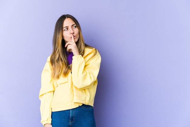 Giovane donna caucasica isolata sulla parete viola mantenendo un segreto o chiedendo silenzio.