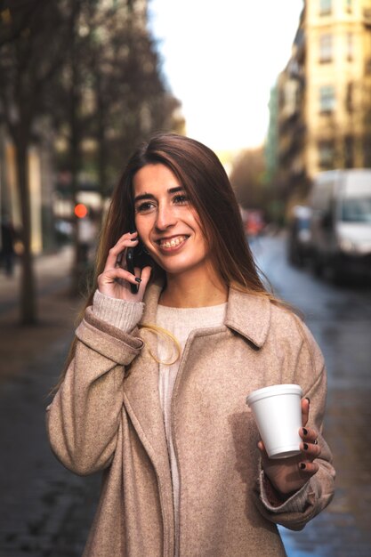 Giovane donna caucasica parlando al telefono mentre beve il caffè