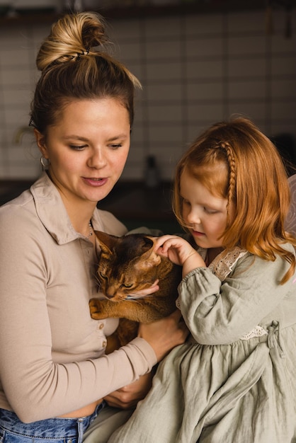 Giovane donna caucasica premurosa che tiene il gatto insieme a una bambina dai capelli rossi all'interno Concetto di stile di vita