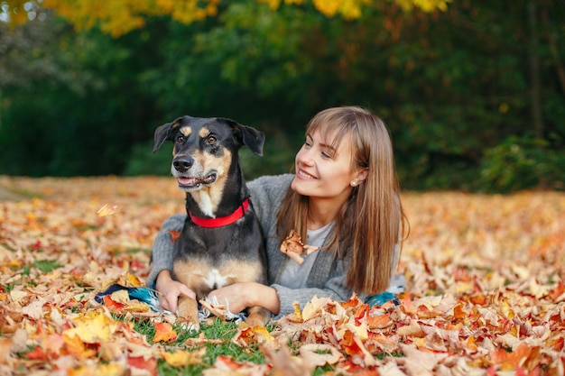 Giovane donna caucasica sdraiata a terra con le foglie cadute abbracciando il proprietario del cane che cammina con l'animale domestico in un giorno d'autunno