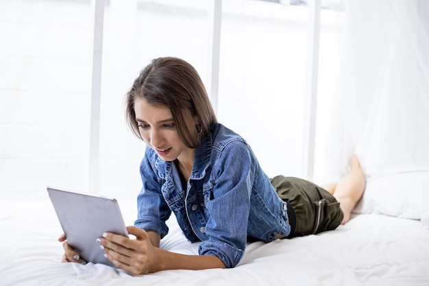Giovane donna caucasica sdraiata accovacciata sul letto che gioca social online in un tablet con felice in camera da letto a casa da sola mentre si rilassa.