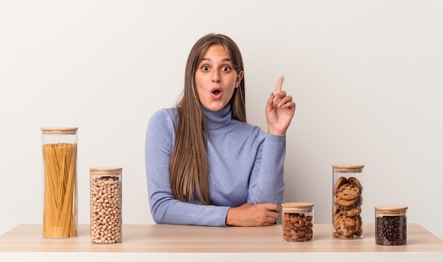 Giovane donna caucasica seduta a un tavolo con un piatto di cibo isolato su sfondo bianco con qualche grande idea, concetto di creatività.