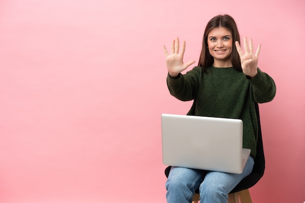 Giovane donna caucasica seduta su una sedia con il suo computer portatile isolato contando nove con le dita