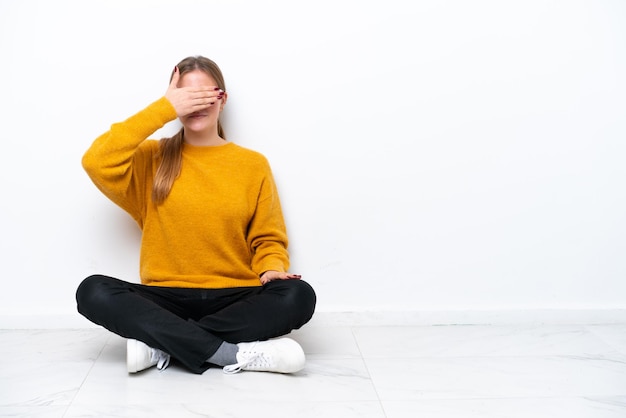 Giovane donna caucasica seduta sul pavimento isolato su sfondo bianco che copre gli occhi con le mani Non voglio vedere qualcosa