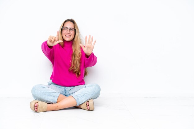 Giovane donna caucasica seduta sul pavimento isolato su sfondo bianco contando sette con le dita