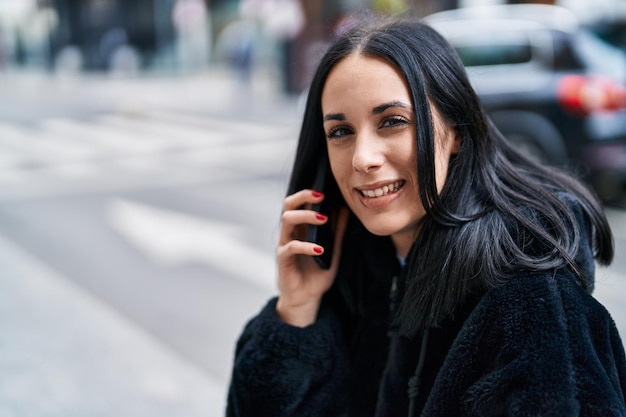 Giovane donna caucasica sorridente parlando fiducioso su smartphone in strada