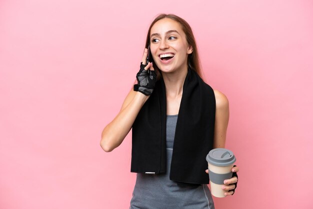 Giovane donna caucasica sportiva che indossa un asciugamano isolato su sfondo rosa che tiene il caffè da portare via e un cellulare