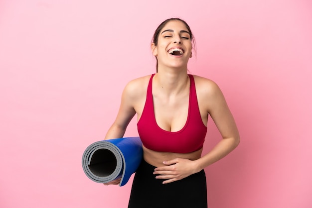 Giovane donna caucasica sportiva che va alle lezioni di yoga mentre tiene in mano un tappetino sorridendo molto