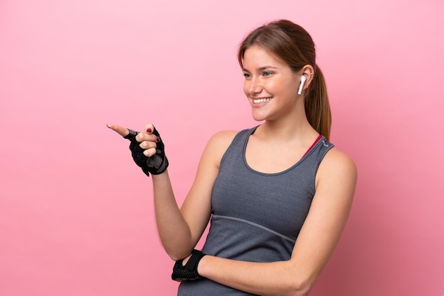 Giovane donna caucasica sportiva isolata su sfondo rosa che punta il dito di lato e presenta un prodotto