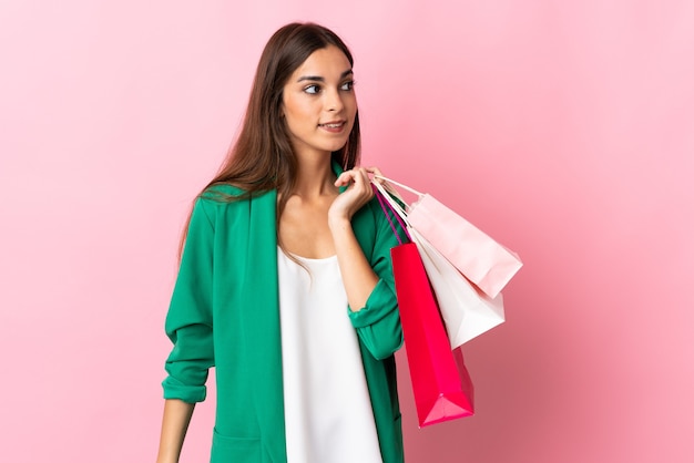 Giovane donna caucasica su rosa tenendo le borse della spesa e guardando indietro