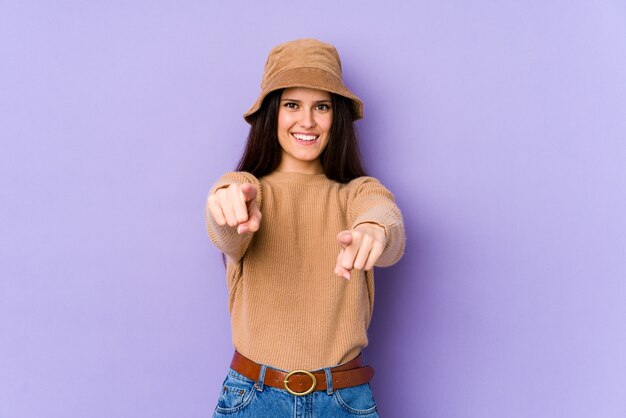Giovane donna caucasica sui sorrisi allegri della parete viola che indica la parte anteriore.