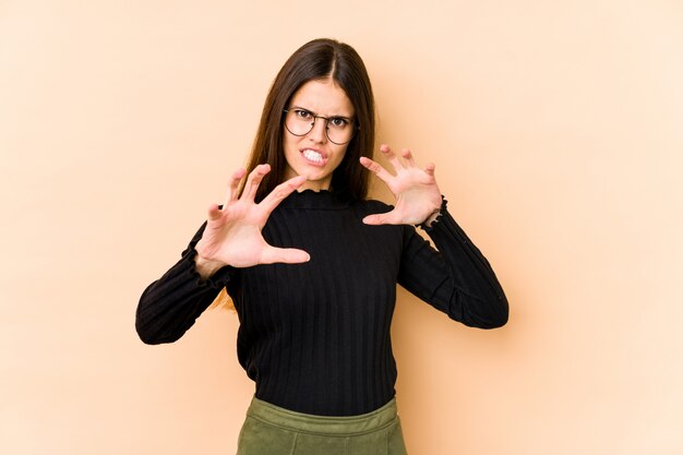 Giovane donna caucasica sul muro beige sconvolto urlando con le mani tese.