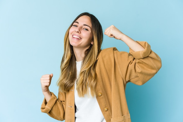 Giovane donna caucasica sull'azzurro che celebra un giorno speciale, salta e alza le braccia con energia.