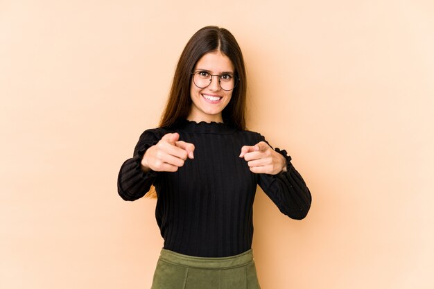 Giovane donna caucasica sull'indicare allegro di sorrisi della parete beige